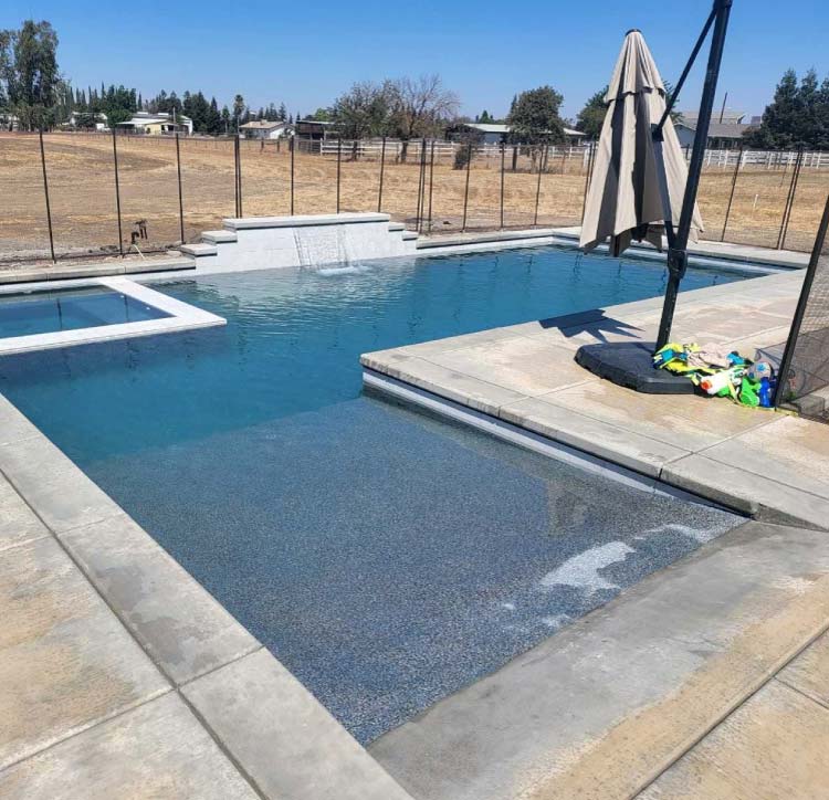 Finished freeform pool with stamped concrete decking and a tiki-style palapa shade structure