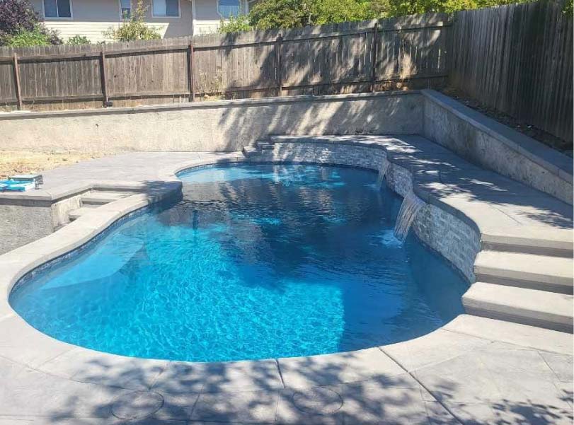 Rectangular pool with wood-look tile coping mid-construction, crew member working poolside