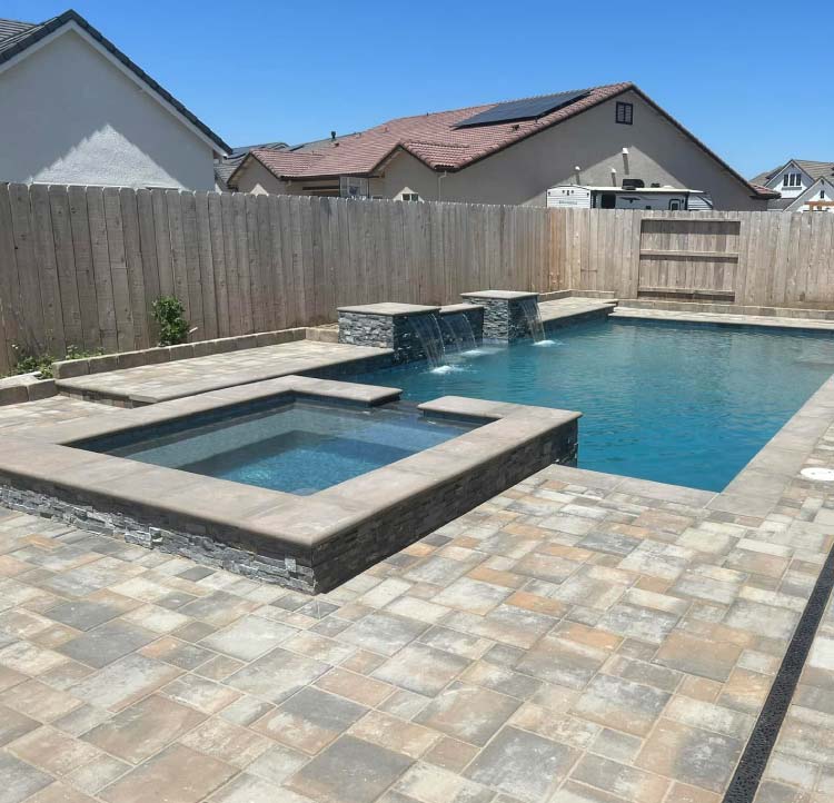 Freeform pool with raised spa and stacked-stone waterfall spillway on a stamped concrete patio