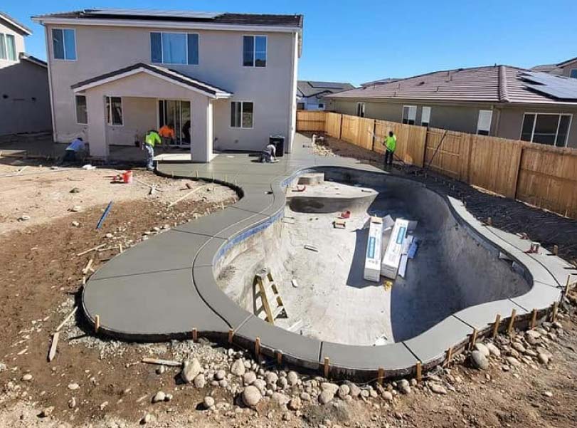 Rectangular pool mid-renovation, drained and showing fresh light blue plaster finish with safety fencing