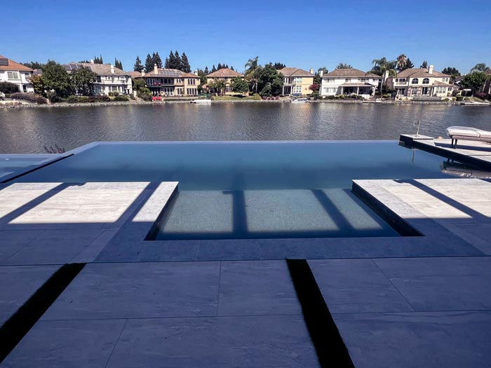 Custom infinity-edge gunite pool overlooking a Sacramento waterfront neighborhood, with tanning ledge and travertine deck by pool contractor atlantic pools and spas