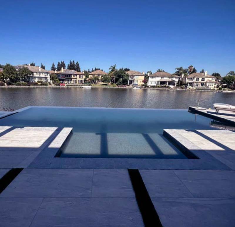 Infinity-edge pool overlooking a Sacramento waterfront neighborhood with travertine deck and tanning ledge